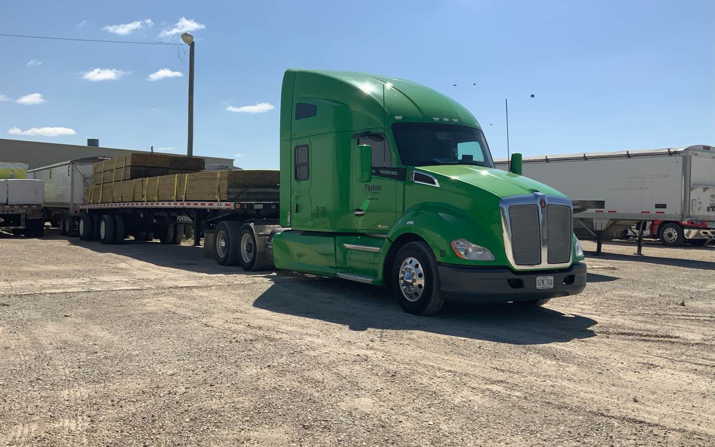 A green Kenworth T680 with a flatbed load of hay, ready to leave the yard