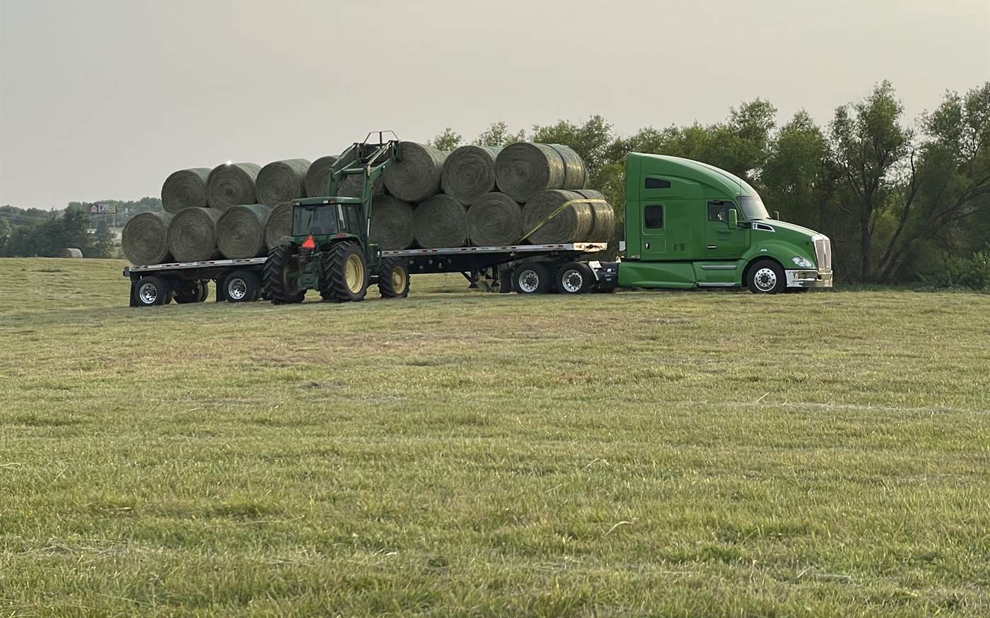 A tractor stacking round bales onto a Tipton flatbed in a hay field