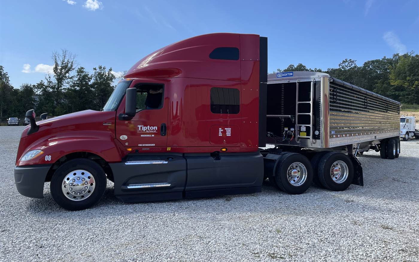 A red Tipton Hay Farms International hooked to a hopper trailer in the yard