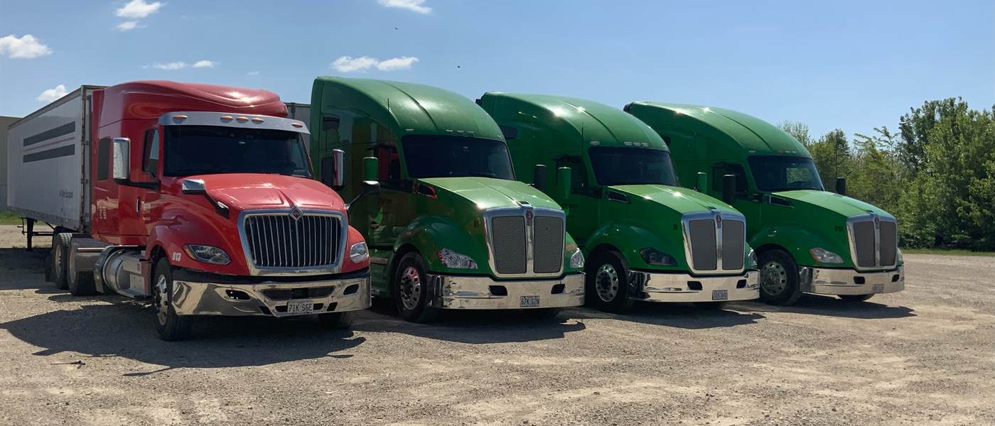 A red International and three green Kenworth T680s lined up in the Tipton Hay Farms yard